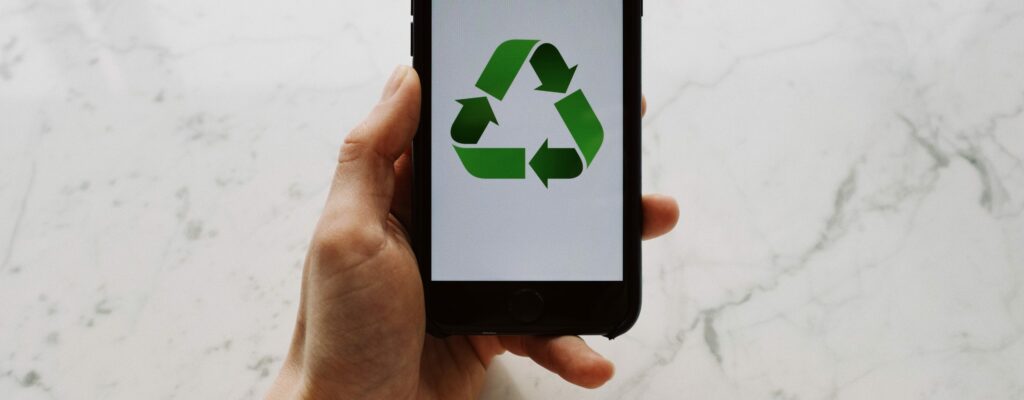 From above view of faceless person holding mobile phone with white screen and green recycle logo above marble surface