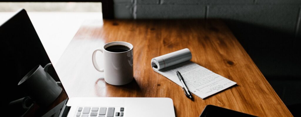 MacBook Pro, white ceramic mug,and black smartphone on table