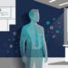 Translucent silhouette of an office worker overlaid with glowing network connections and app icons drifting into the shadows, representing shadow AI use inside a business